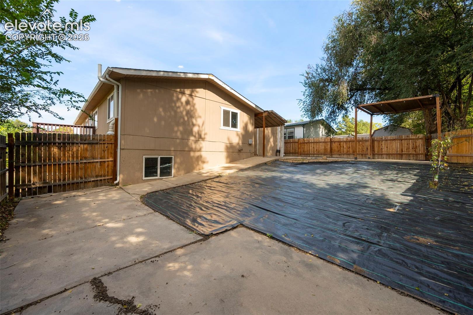 Rear exterior featuring a concrete patio, wood privacy fencing, a metal-frame pergola, and mature shade trees