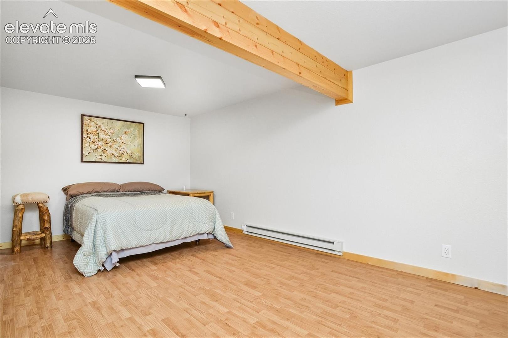 Spacious room featuring wood-finish flooring, white walls, and an exposed wood beam ceiling detail