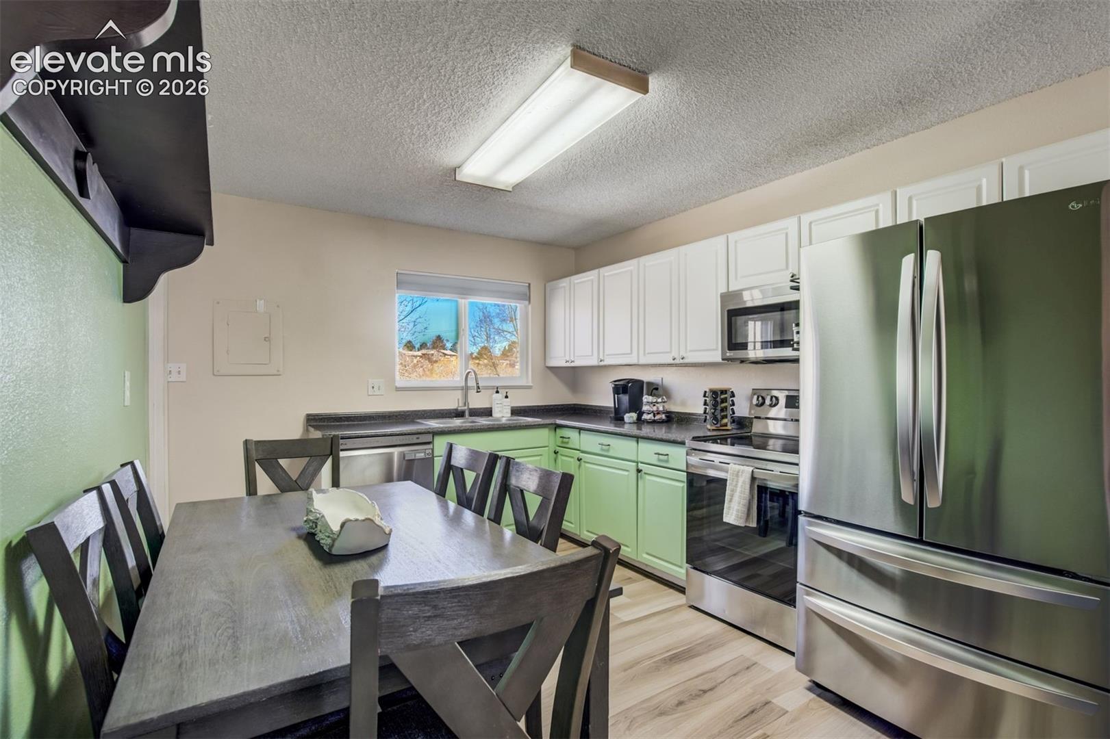 Kitchen with dual-tone cabinetry, stainless steel appliances, dark countertops, a stainless steel sink, and light wood-finish flooring