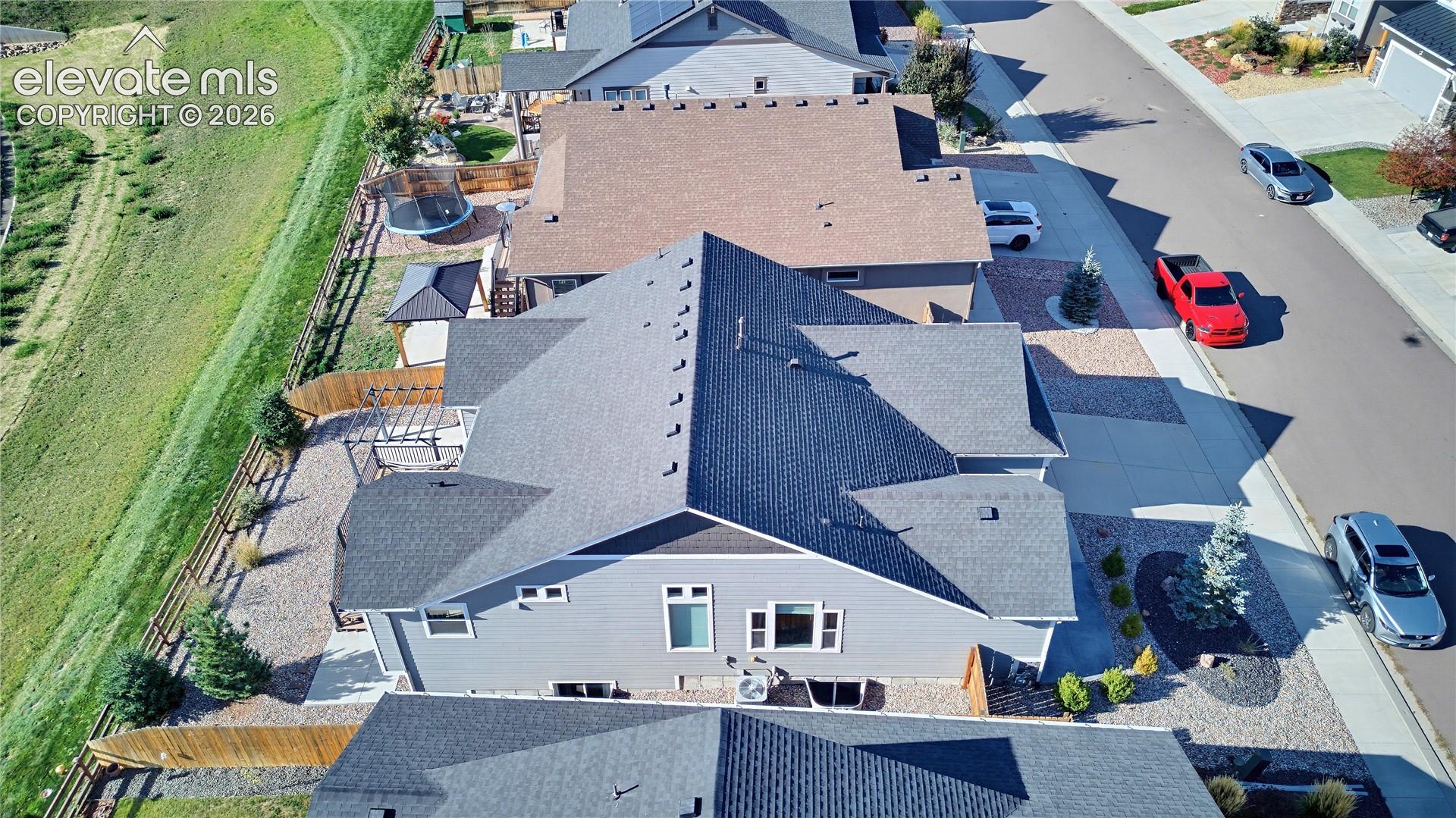 Aerial perspective of a multi-gabled residence featuring horizontal siding, a concrete driveway, a fenced backyard, and surrounding open space
