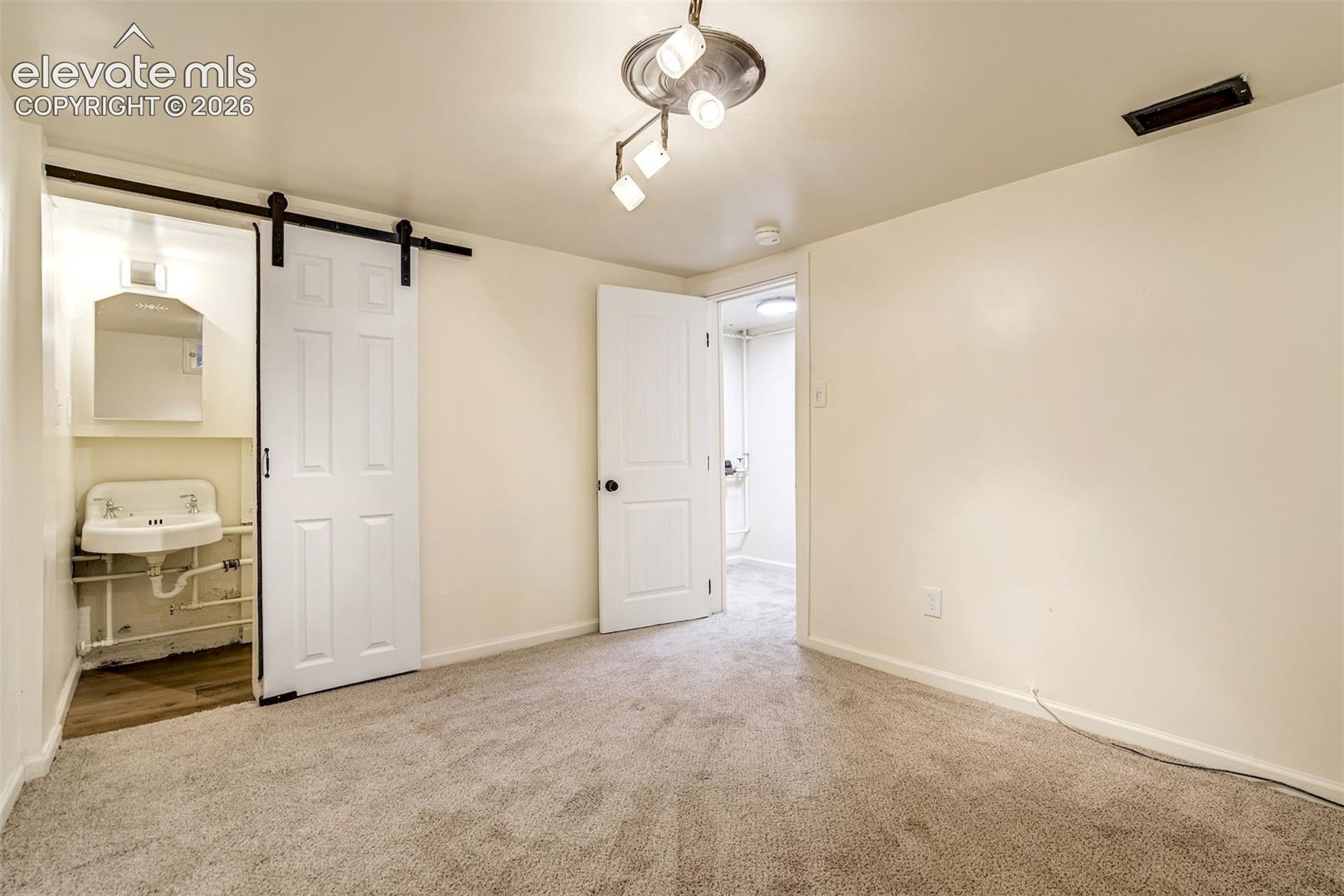 Interior space featuring neutral wall-to-wall carpeting, a sliding barn door, wall-mounted sink with mirror, multi-directional ceiling lighting, and a paneled interior door