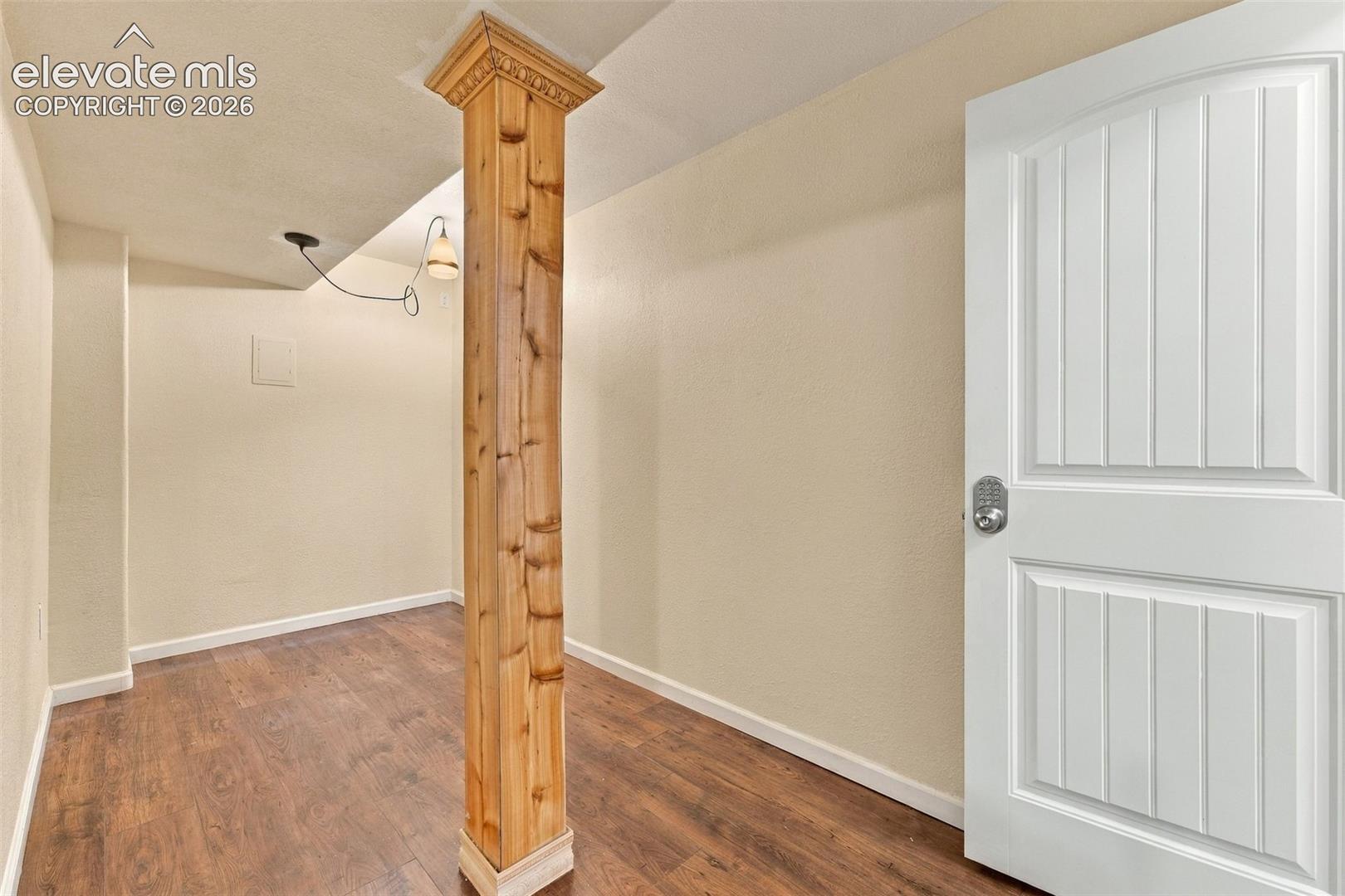 Structural wood-finish post with crown molding detail, wood-finish flooring, and white two-panel interior door
