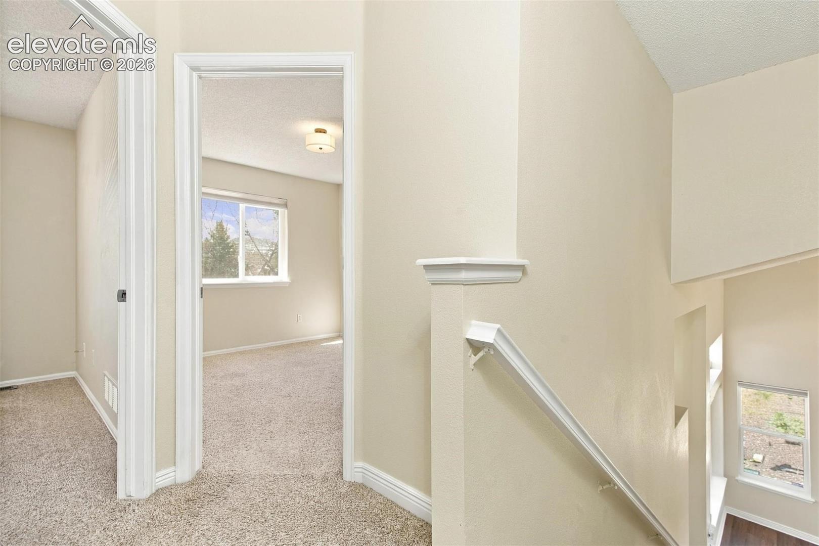Neutral-toned interior featuring wall-to-wall carpeting, white millwork trim, recessed lighting, and a partial staircase with a white handrail