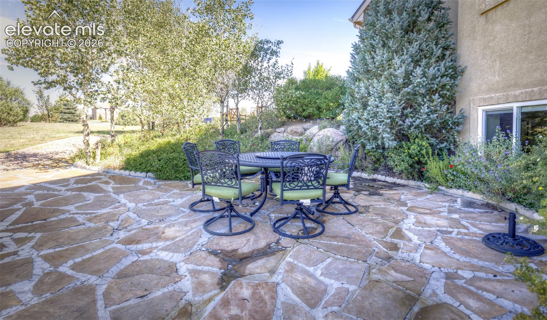 Flagstone patio with a stucco exterior, mature evergreen, and varied foliage