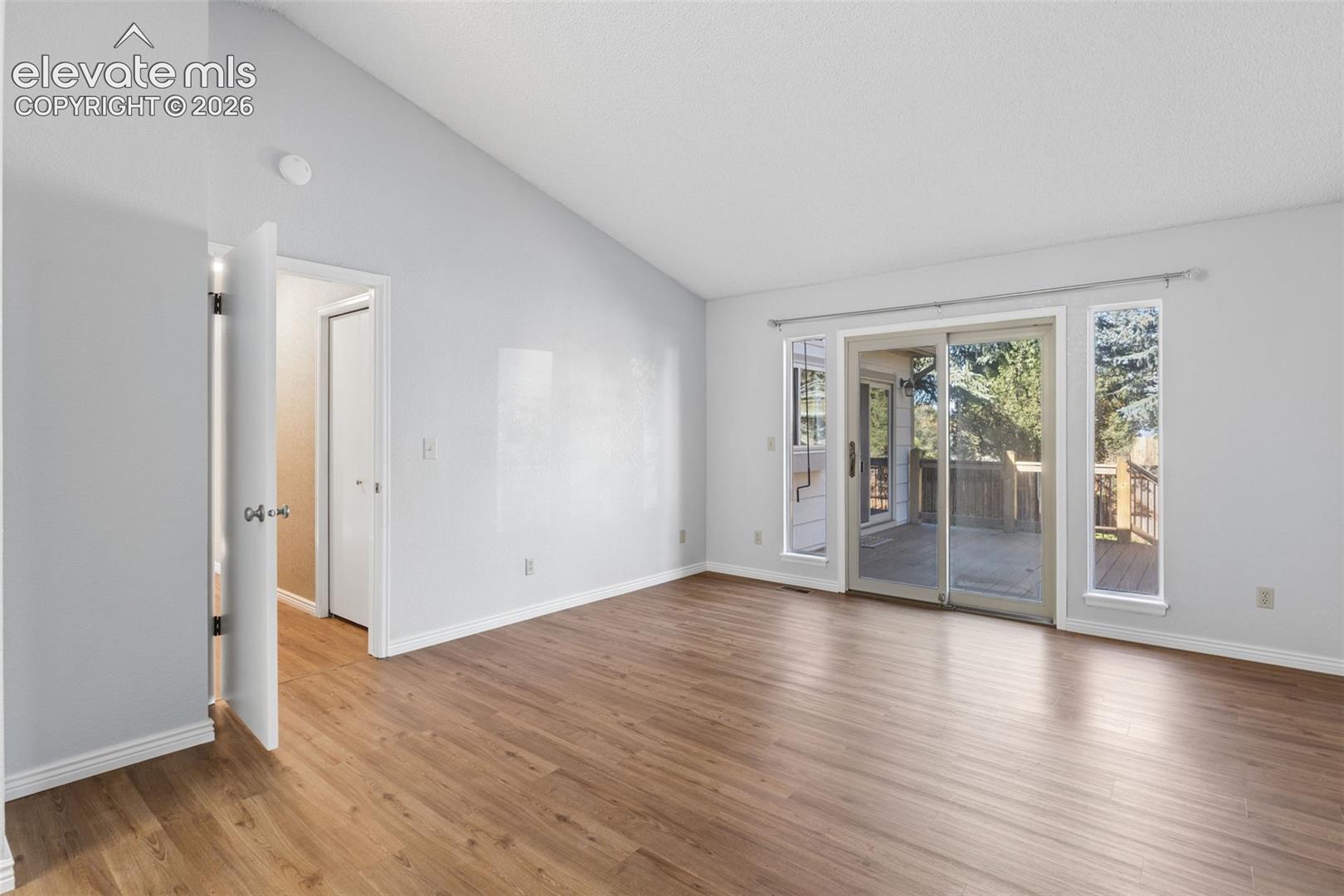 Room featuring a vaulted ceiling, wood-finish flooring, and sliding glass doors with sidelights