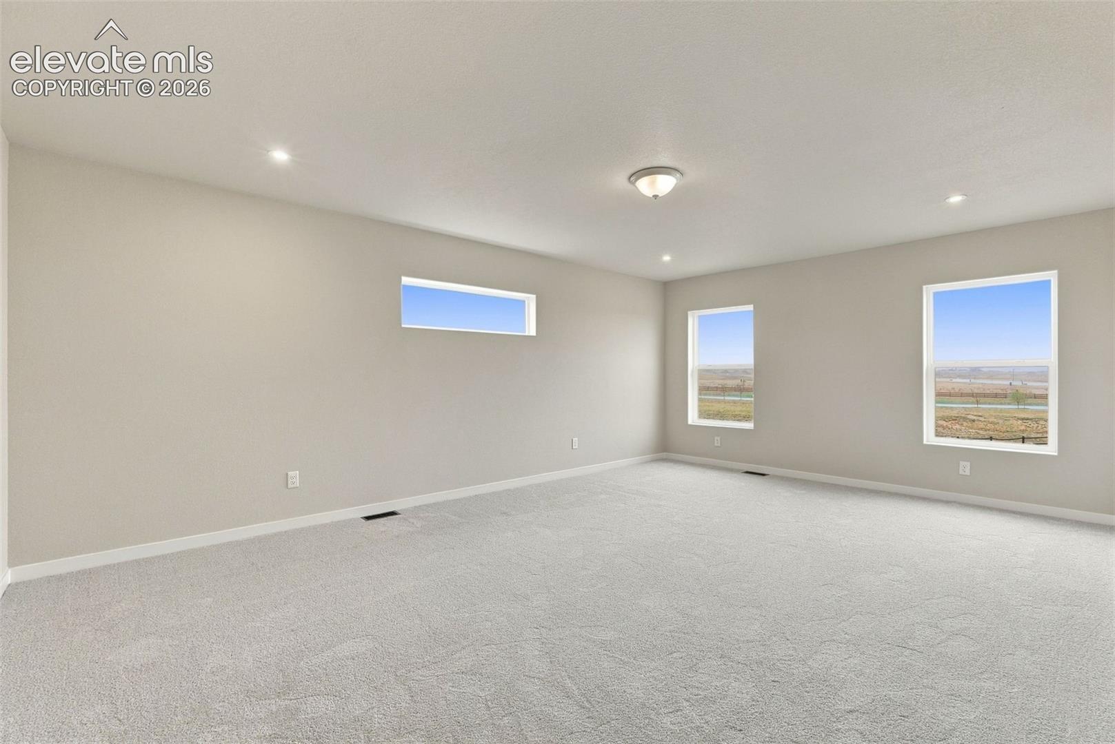Neutral-toned interior space featuring wall-to-wall carpeting, recessed ceiling lighting, a flush-mount fixture, two full-sized windows, and a horizontal transom window