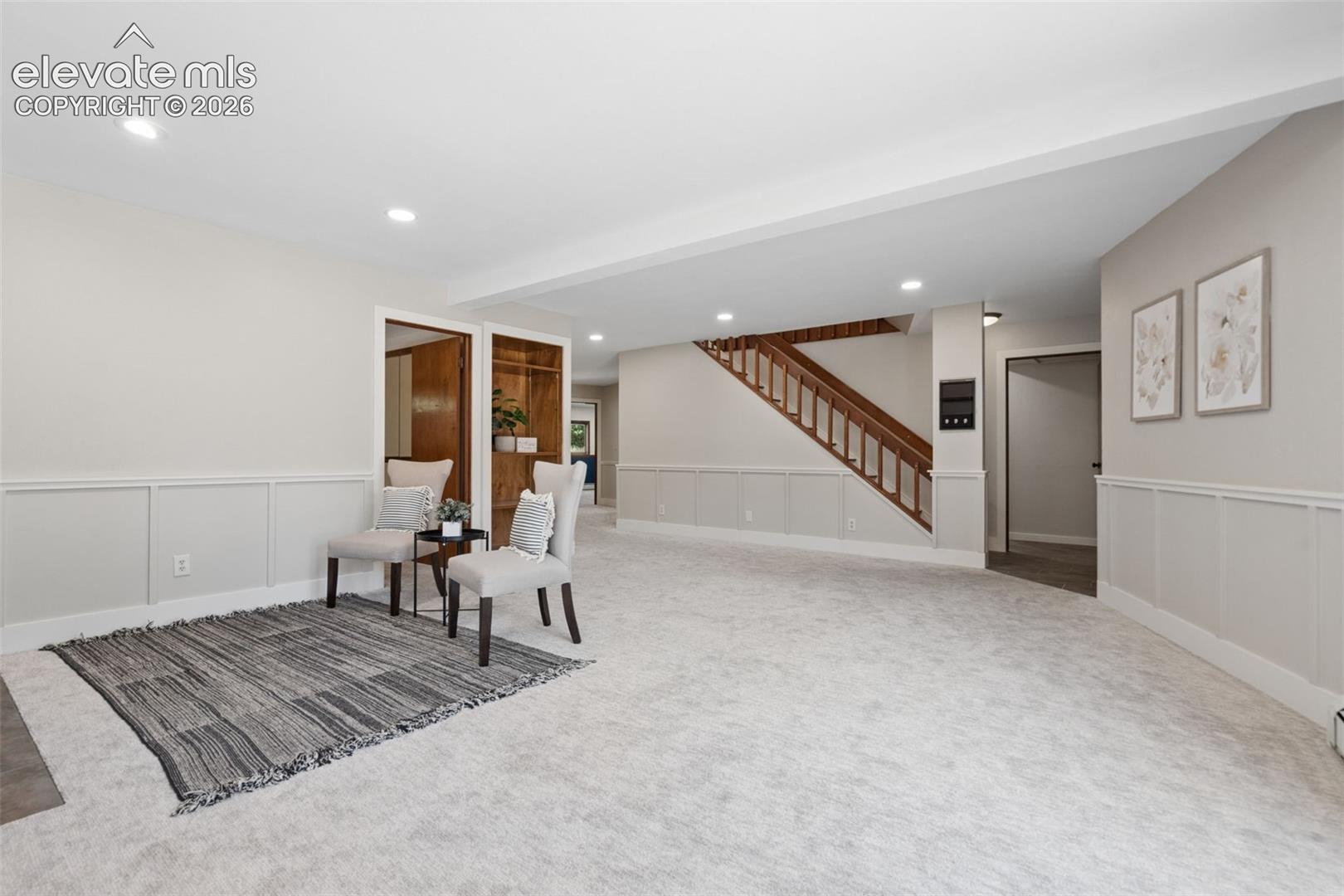 Expansive carpeted room with recessed lighting, wainscoting, and wood-finish open shelving