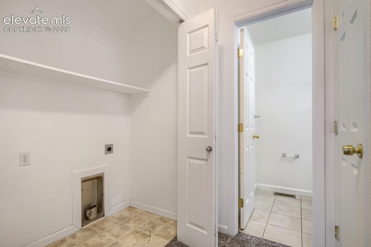 Utility space featuring built-in shelving, tile flooring, and dedicated washer and dryer hookups, with a six-panel door entry