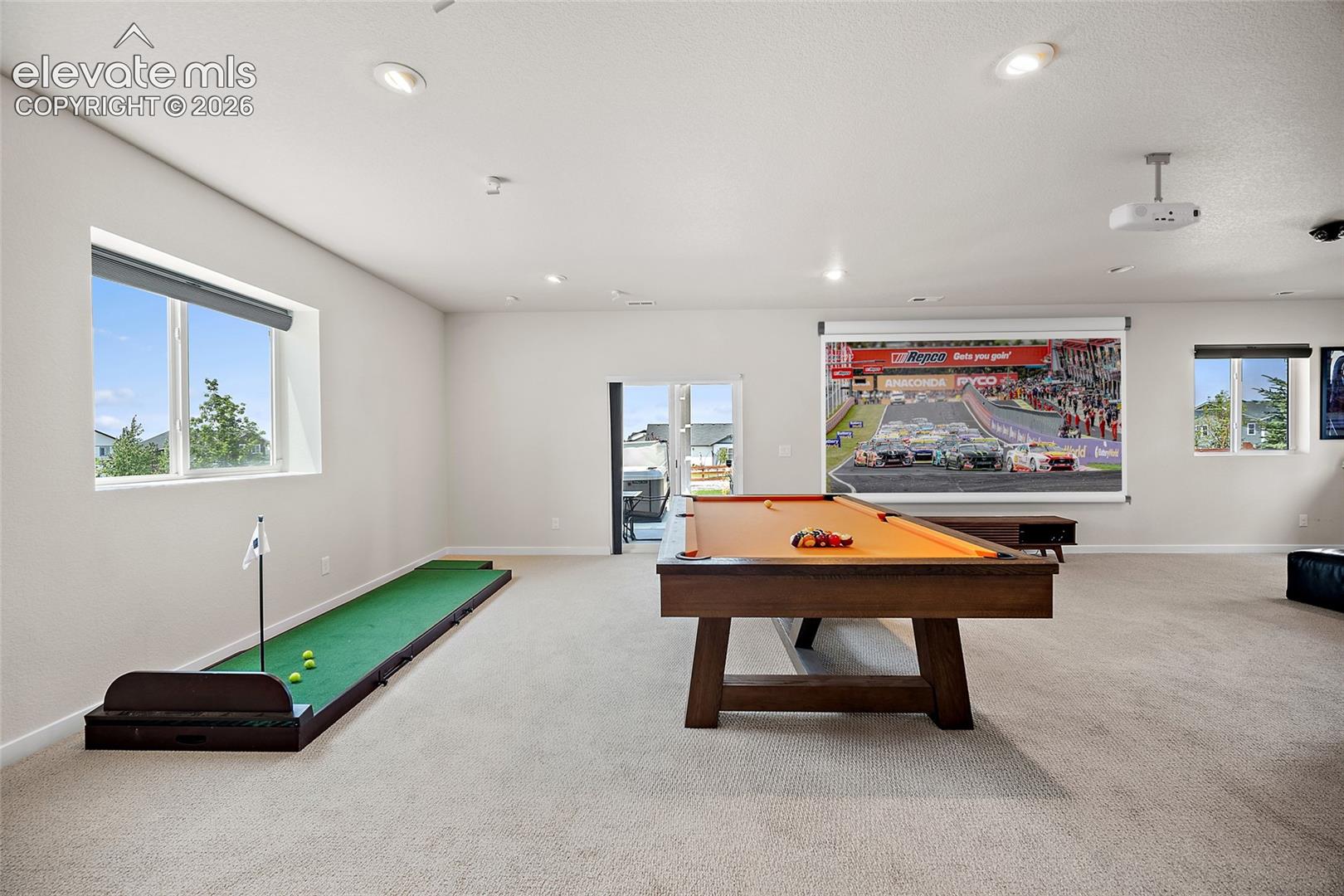 Spacious entertainment room featuring recessed lighting, projector, screen, and a sliding glass door