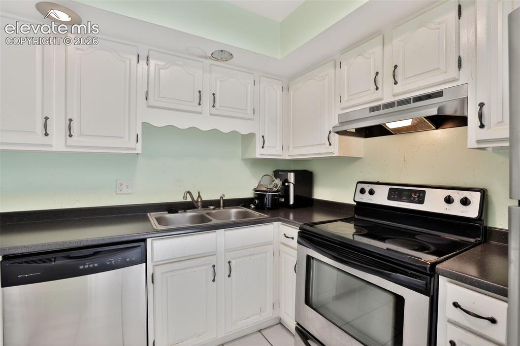 Kitchen featuring white cabinetry, dark countertops, a double basin stainless steel sink, a stainless steel range with an overhead vent, and a stainless steel dishwasher