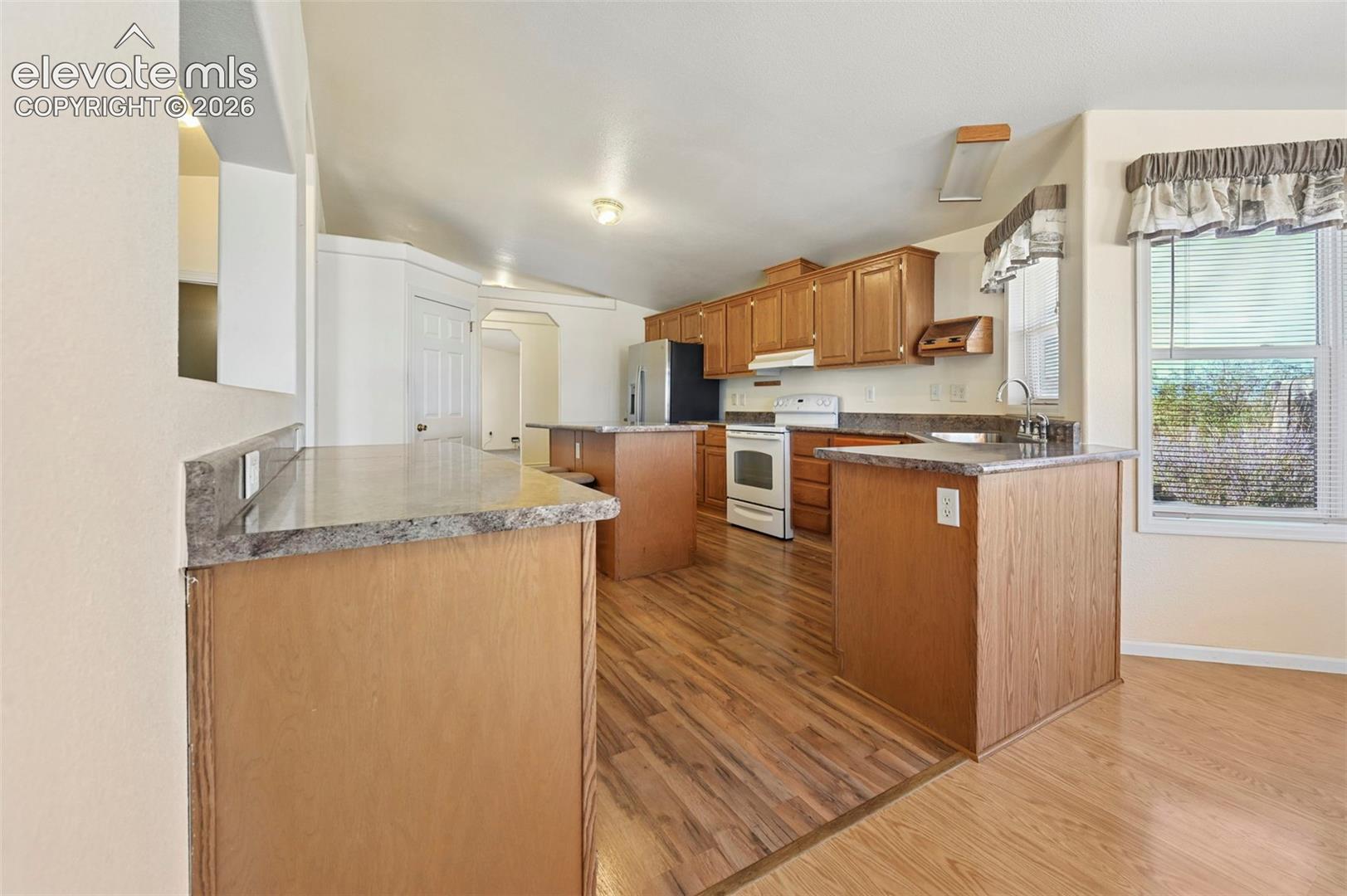 Kitchen featuring wood cabinetry, laminate countertops, a central island, and wood-finish flooring