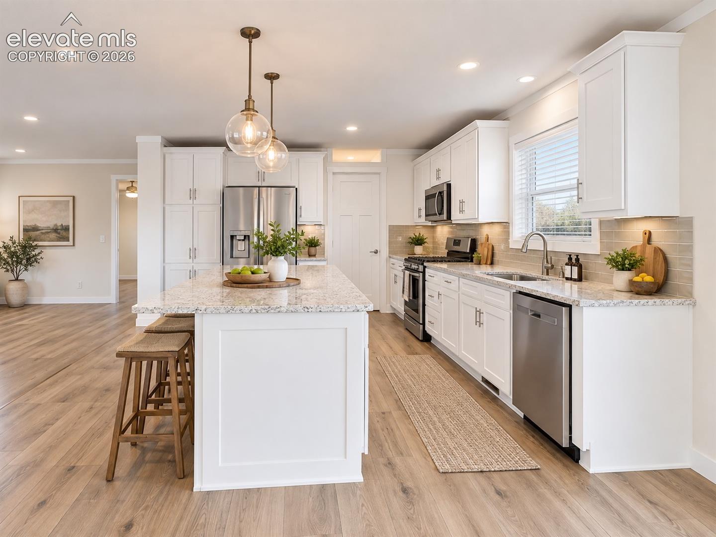 Bright, open kitchen featuring white shaker-style cabinetry, expansive countertops, stainless steel appliances, and a large center island with breakfast-bar seating.