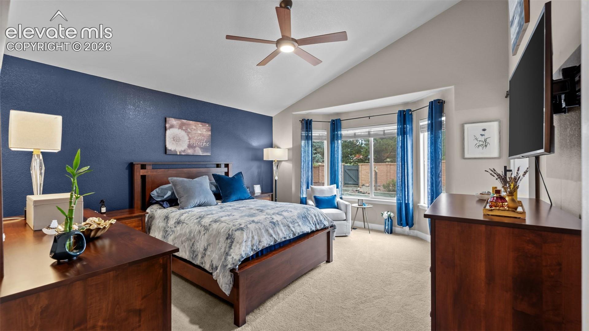 Vaulted ceilings, bay window, ceiling fan with integrated lighting, and neutral carpeting