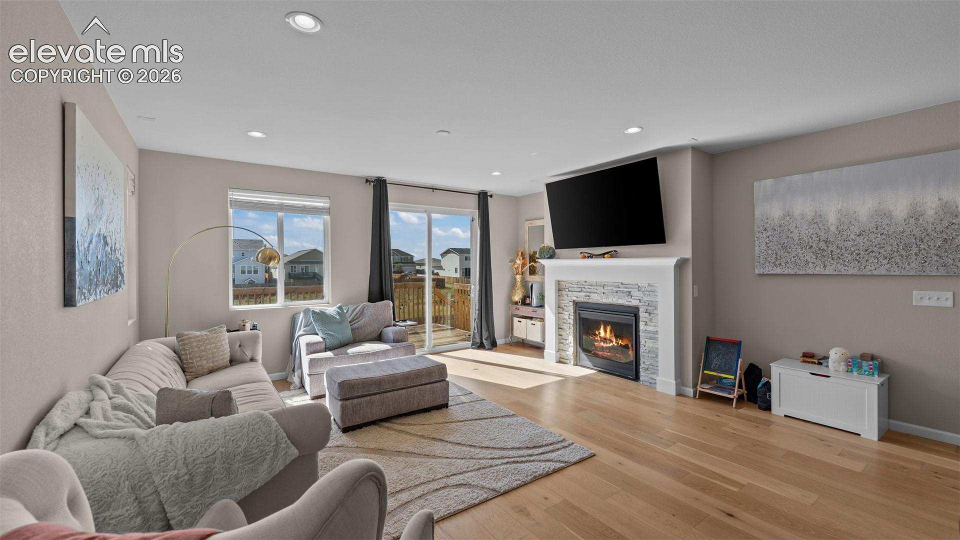 Wood-finish flooring, recessed lighting, and a fireplace with a stone surround
