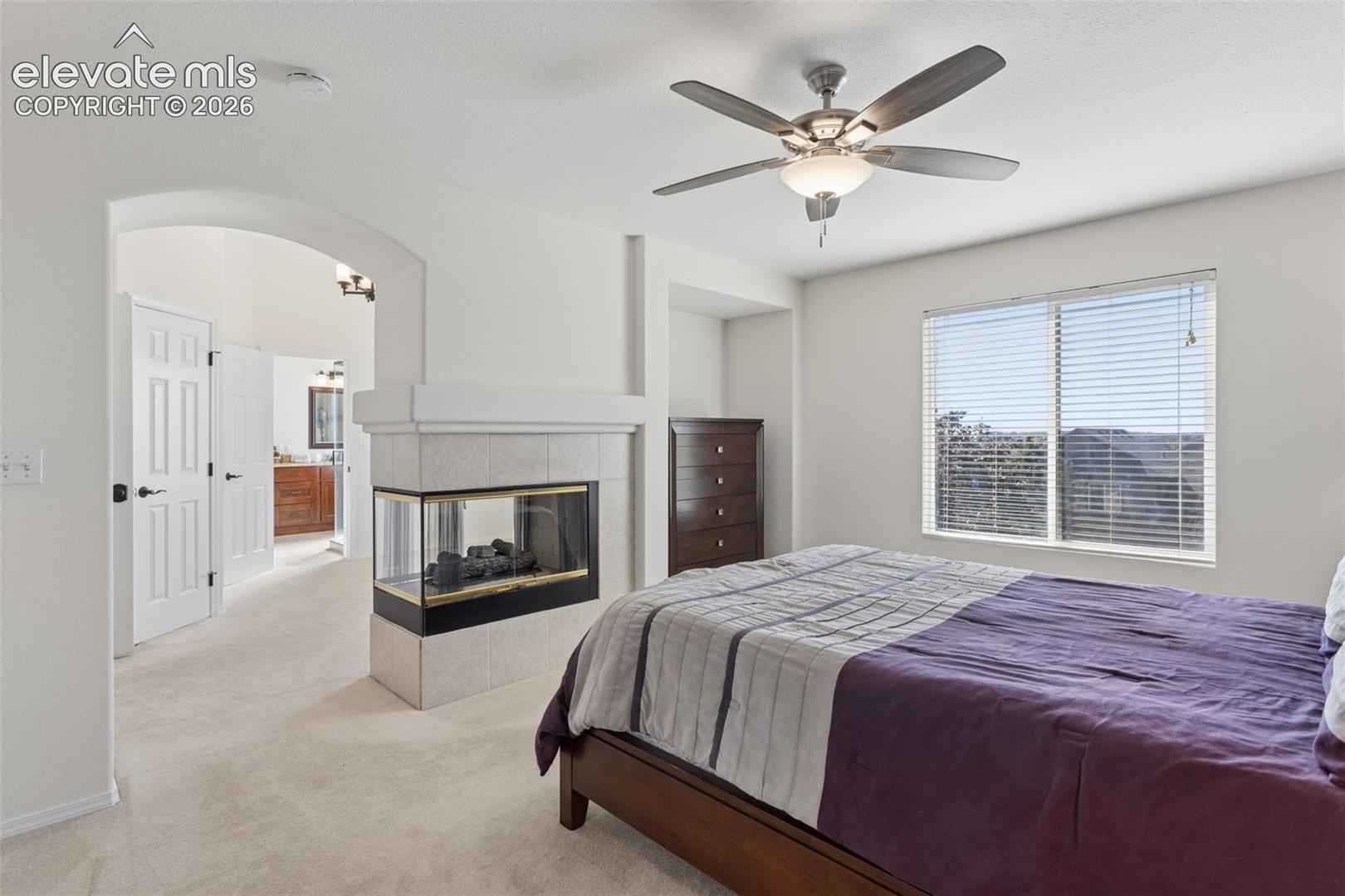 Primary bedroom with double-sided fireplace featuring tile surround between adjacent master retreat/office room 