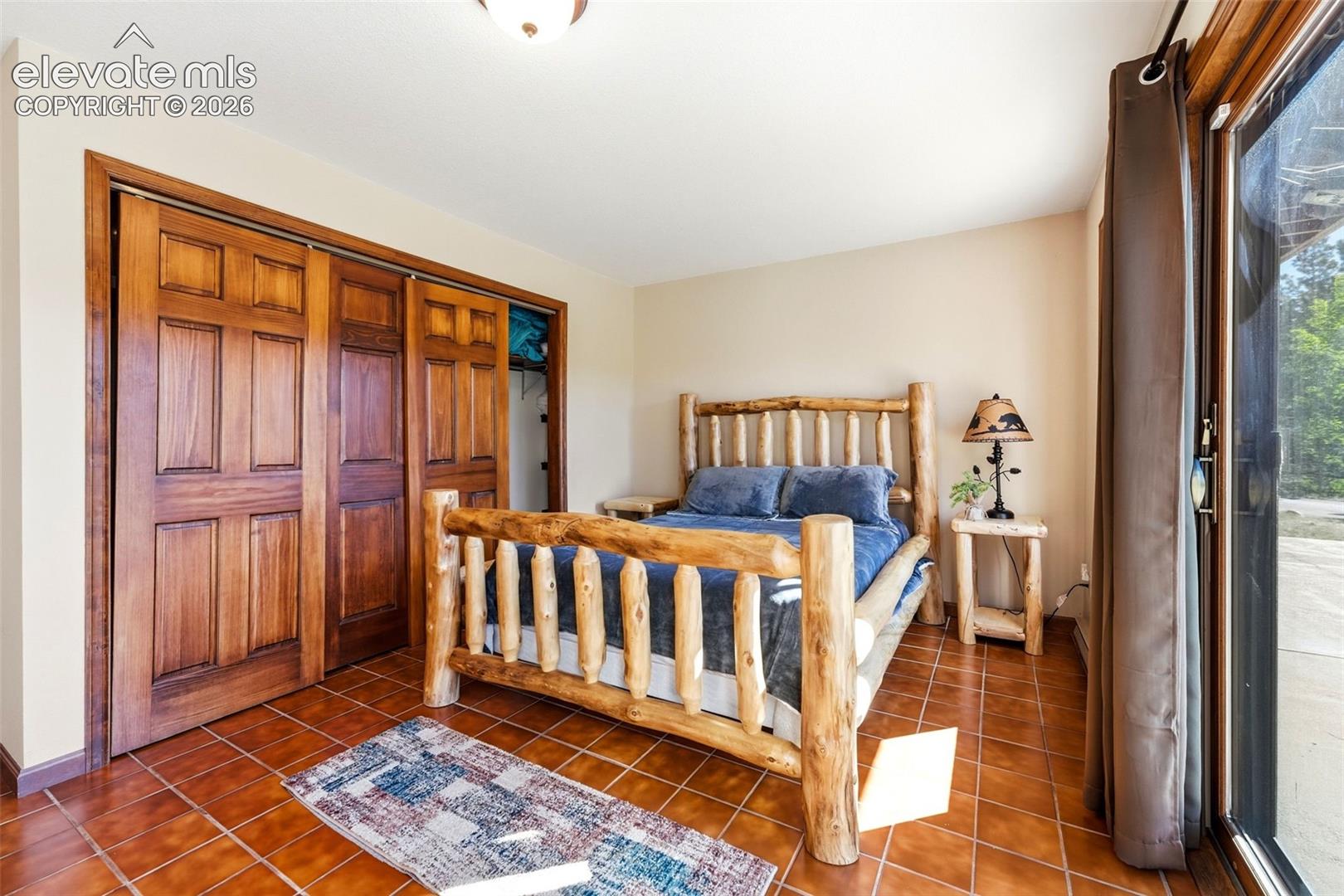 Terracotta tile flooring, wood-paneled sliding closet doors, ceiling-mounted light fixture, and glass patio door