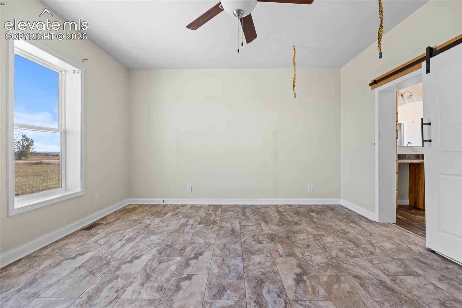 Room featuring wood-finish tile flooring, a sliding barn-style door, ceiling fan, and large double-hung window