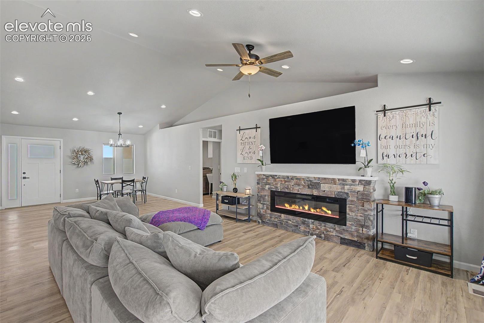 Living room featuring wood-finish flooring, a stone-faced electric fireplace with a white mantel, and a vaulted ceiling with recessed lighting