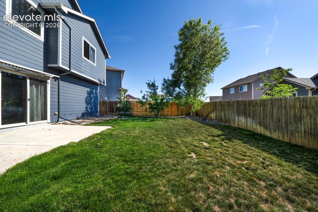 Rear exterior featuring horizontal lap siding, a concrete patio, a fenced yard, and a grass lawn