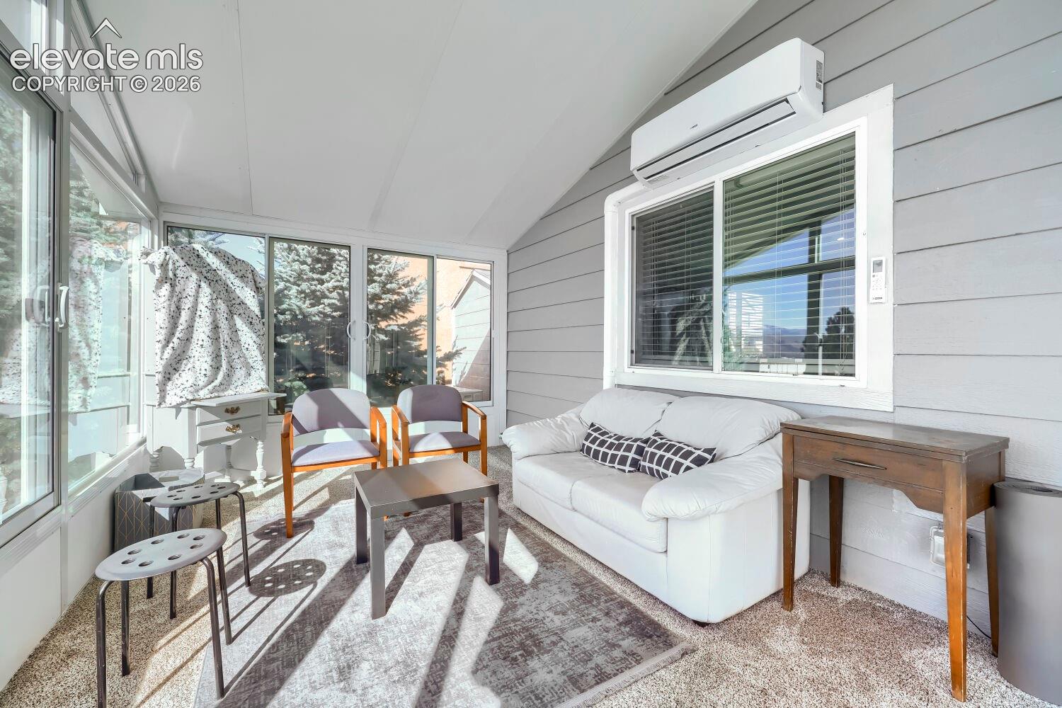 Enclosed sunroom featuring expansive windows, horizontal lap siding, and a wall-mounted ductless heating and cooling unit