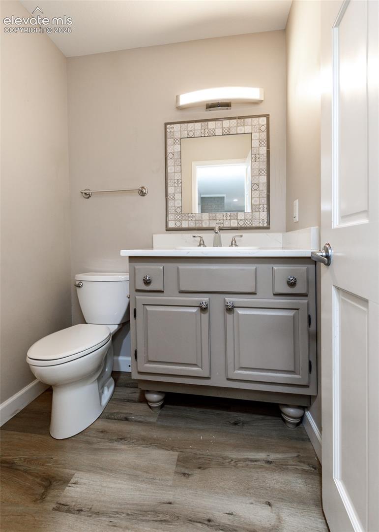 Gray vanity with white countertop and integrated sink, mosaic-framed mirror, contemporary light fixture, and wood-finish flooring