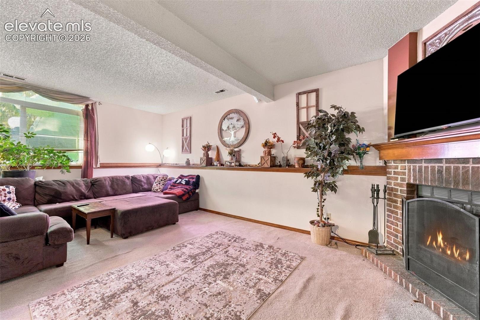 Brick fireplace with a wood mantel, wood-trimmed chair rail, and wall-to-wall carpeting