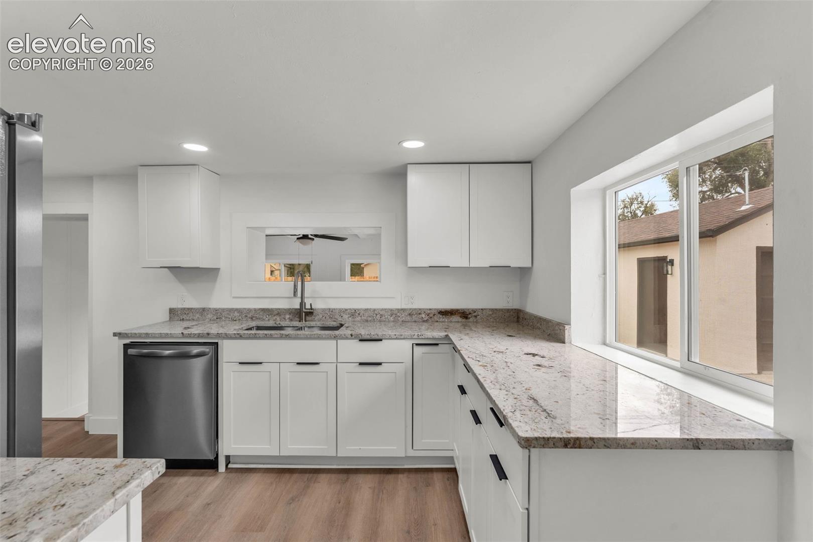 Kitchen featuring white shaker-style cabinetry, stone-finish countertops, stainless steel dishwasher, wood-finish flooring, and recessed ceiling lighting