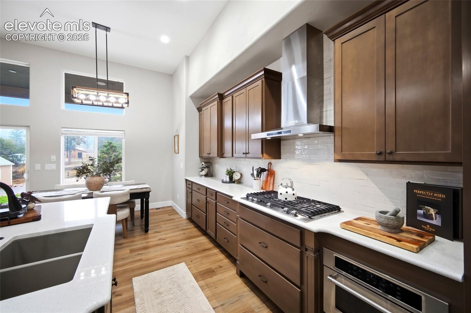 Kitchen featuring shaker-style cabinetry, stainless steel range hood, stone-finish countertops, wood-finish flooring, and high ceilings