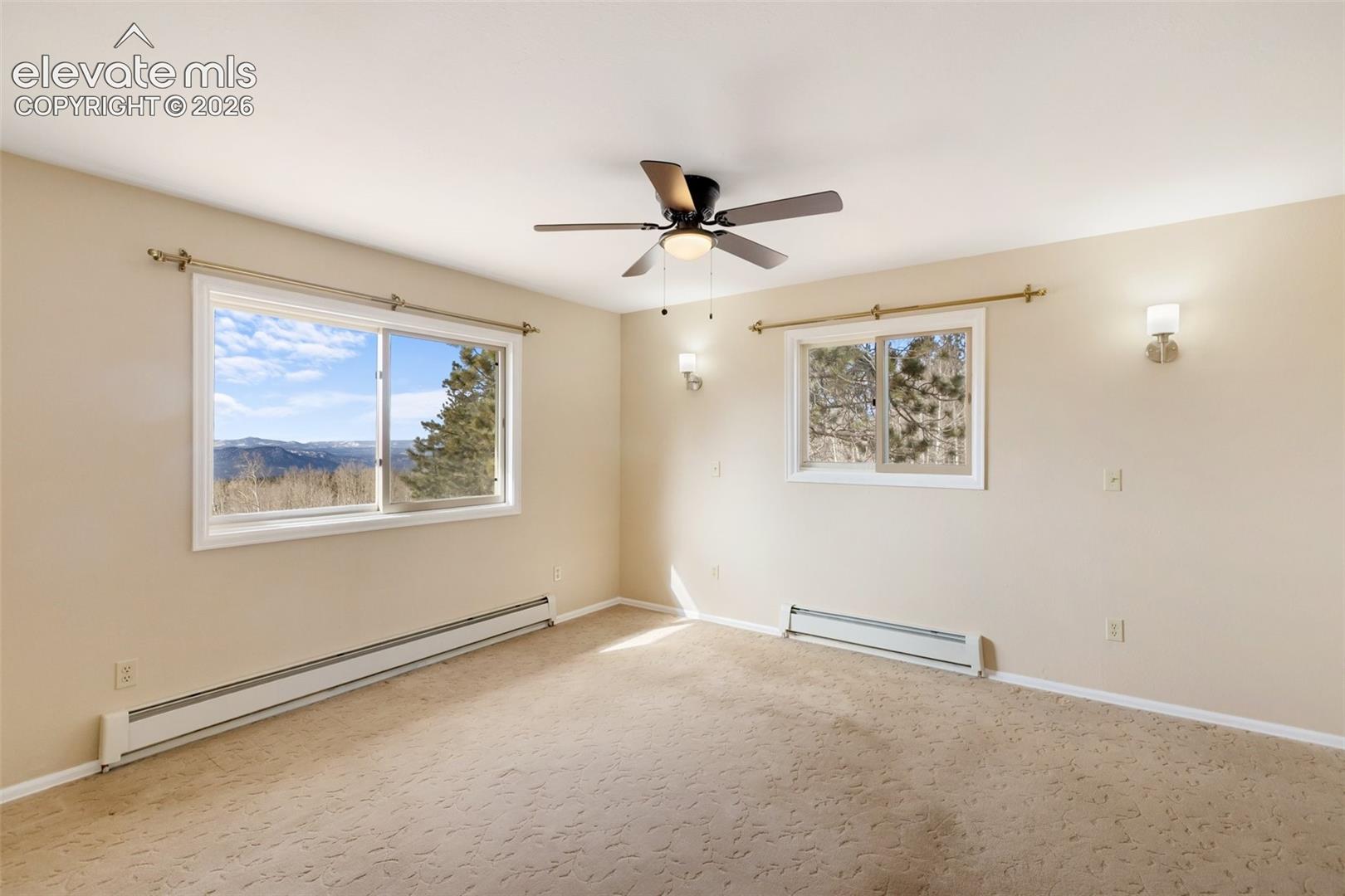 Wall-to-wall carpeted room with multiple windows, a ceiling fan, and wall sconces