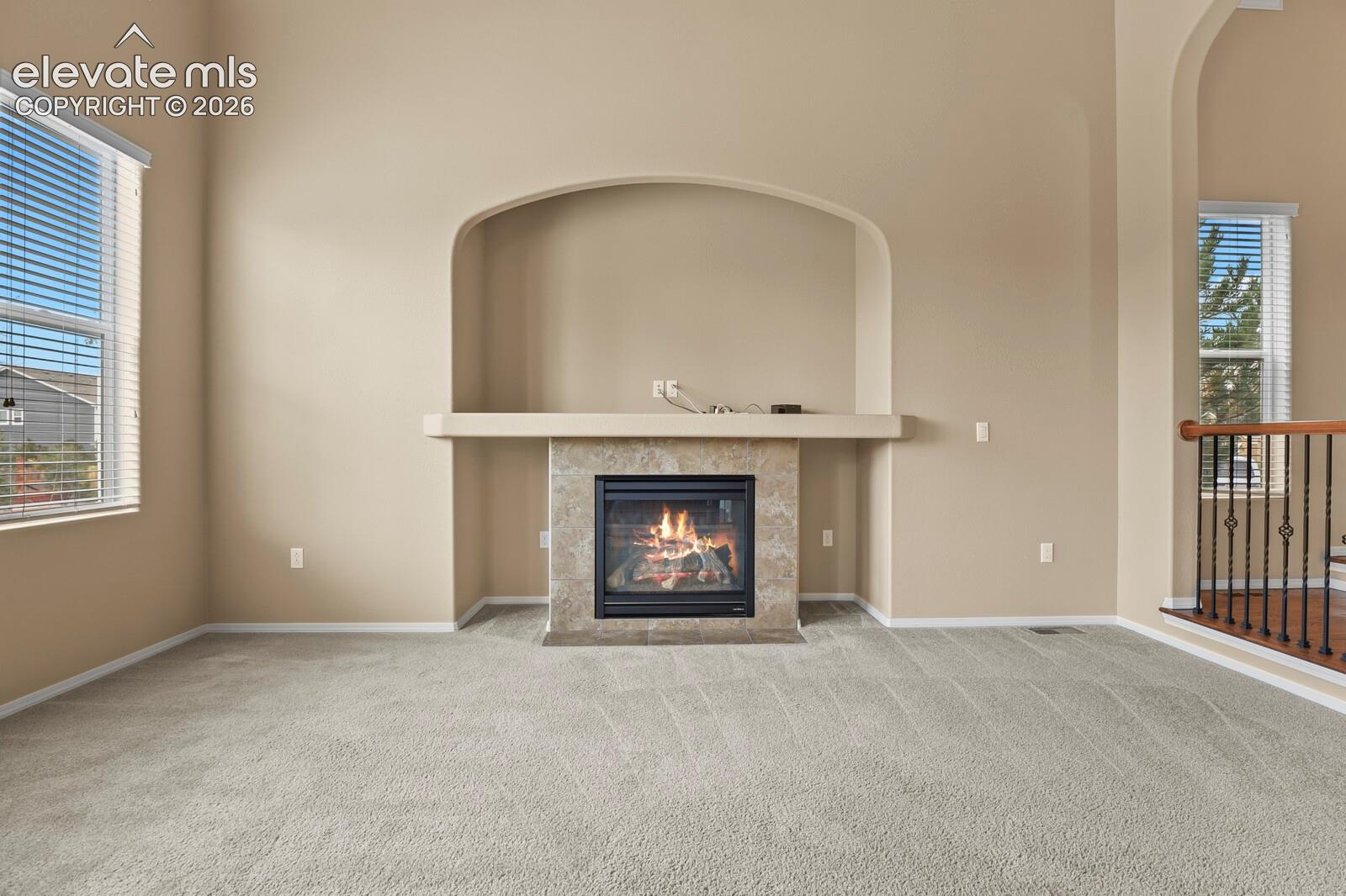 Recessed fireplace with a tile surround and mantel, arched wall niche, neutral wall color, light-toned carpet flooring, and window blinds