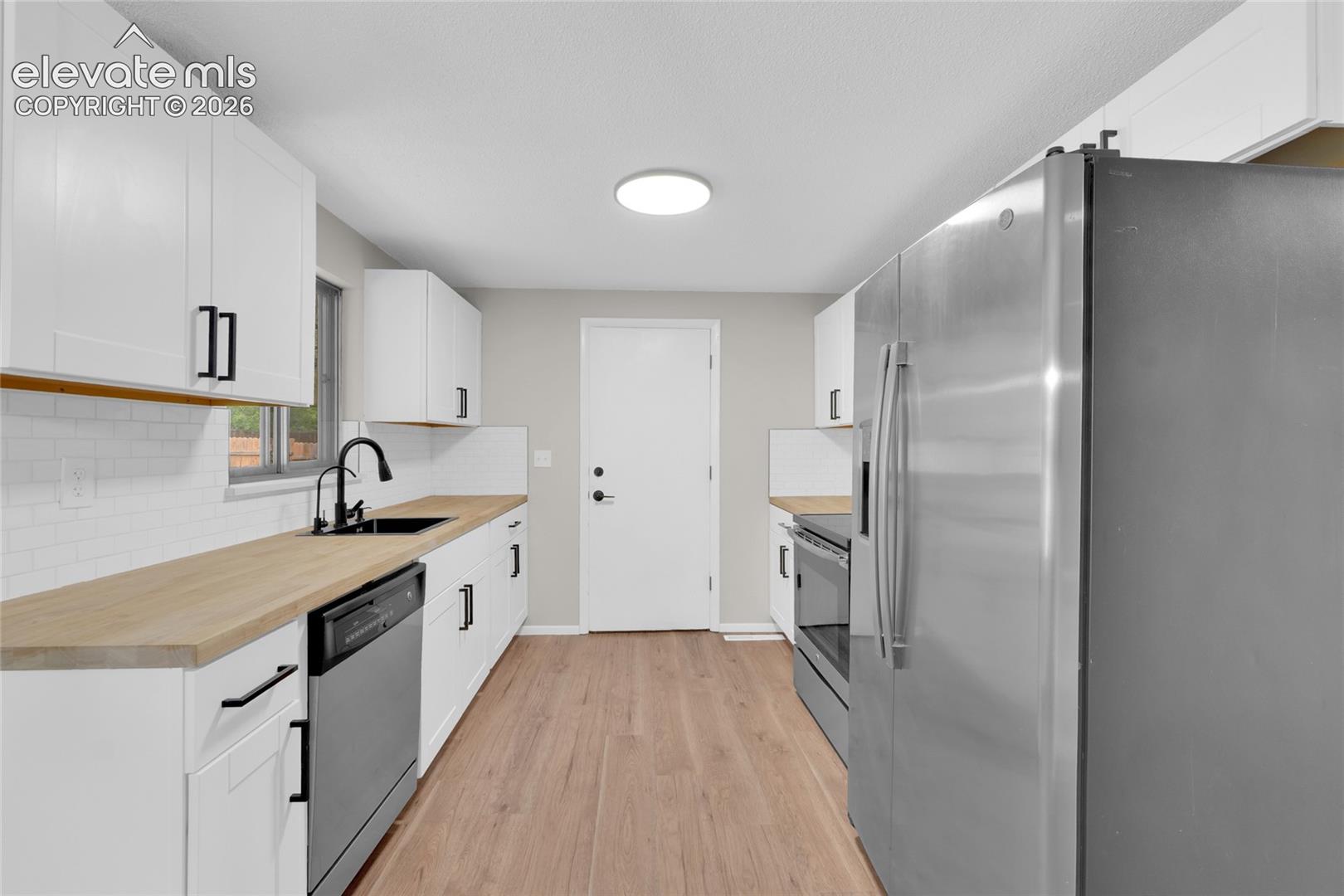 Kitchen featuring wood-finish flooring, white cabinetry with matte black hardware, wood countertops, a subway tile backsplash, and stainless steel appliances