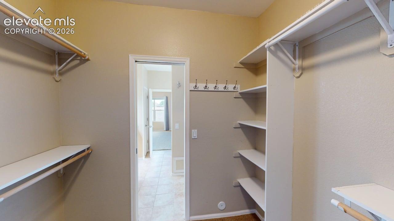 Walk-in closet featuring white shelving, multiple hanging rods, and wall-mounted hooks