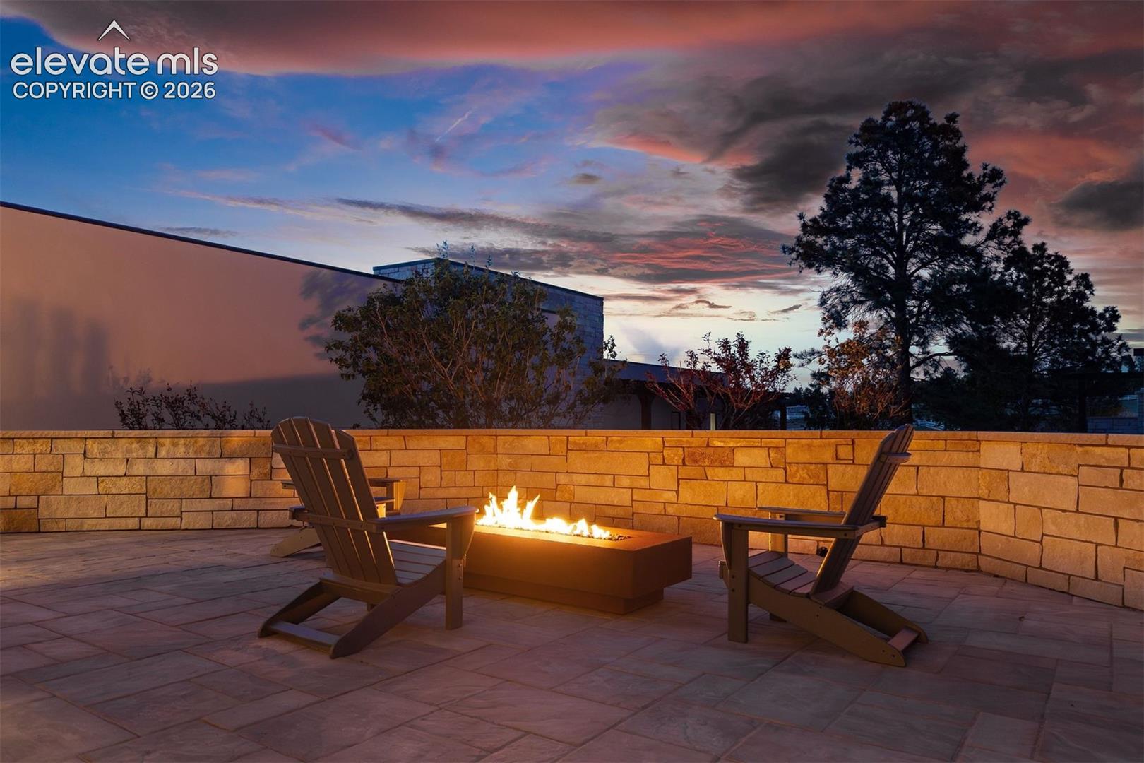 Stunning courtyard patio with a sleek linear Corten steel gas fire pit framed by a stacked stone privacy wall. 