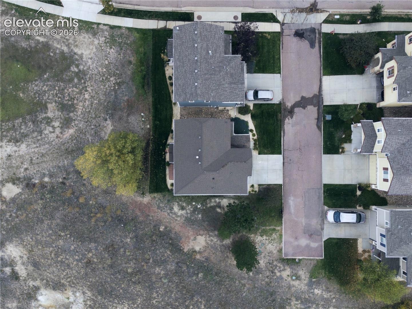 Aerial perspective of the property featuring a concrete driveway, multi-gabled roofline, and established greenery