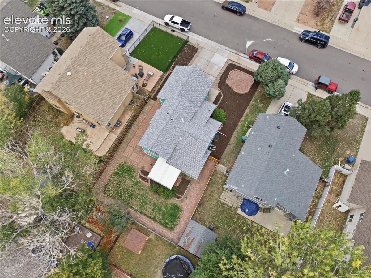 Aerial perspective of the property featuring a gabled roofline, masonry patio, defined landscaping beds, and an enclosed backyard area