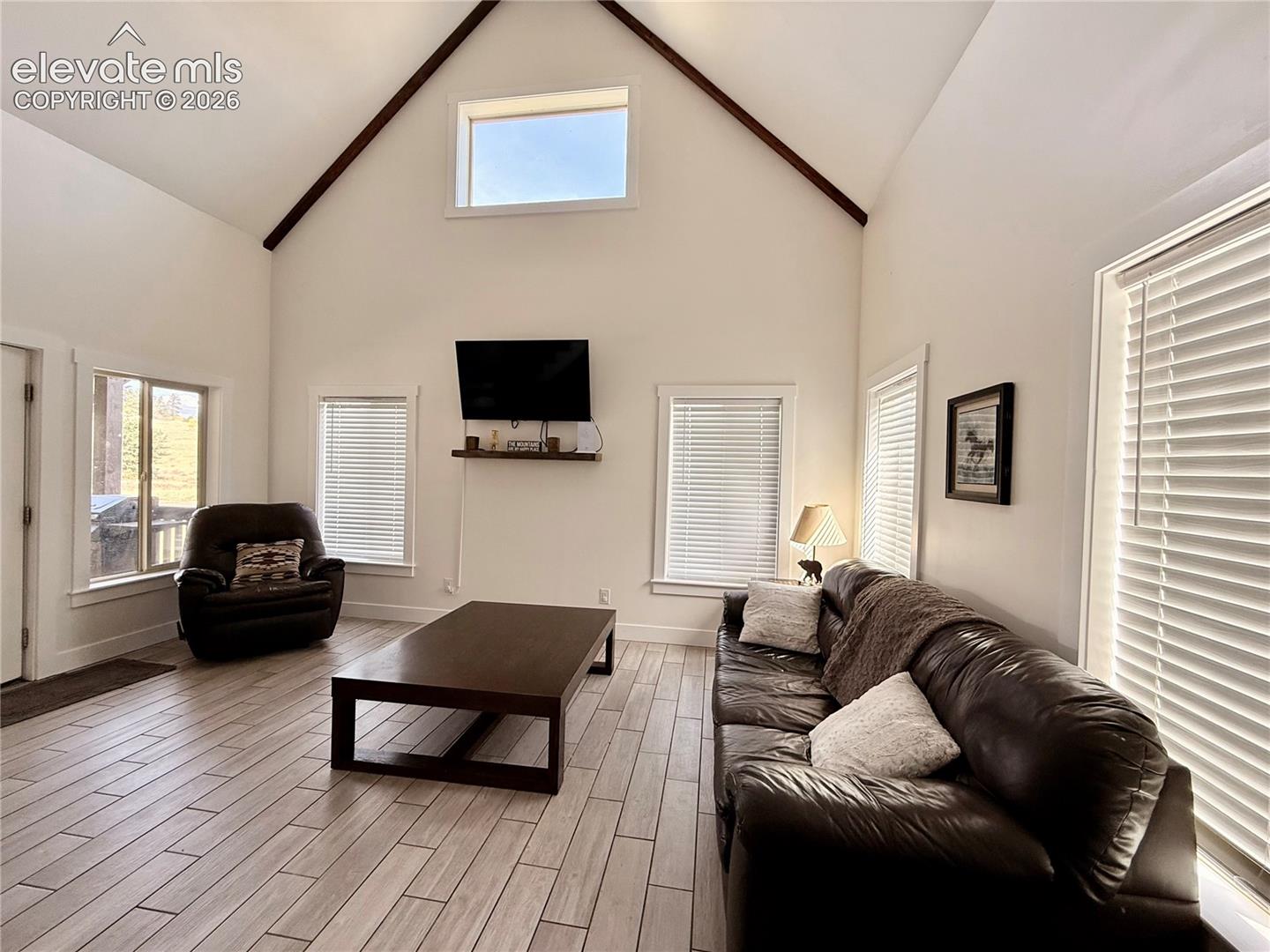 Vaulted ceiling, exposed ceiling beams, upper clerestory window, wood-finish flooring, multiple windows with blinds