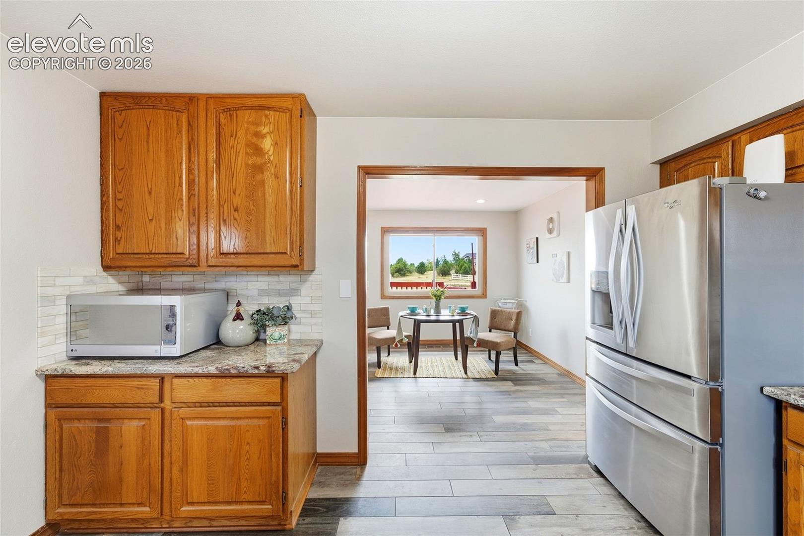 Wood-finish flooring, wood cabinetry, stone-finish countertops, and a white subway tile backsplash
