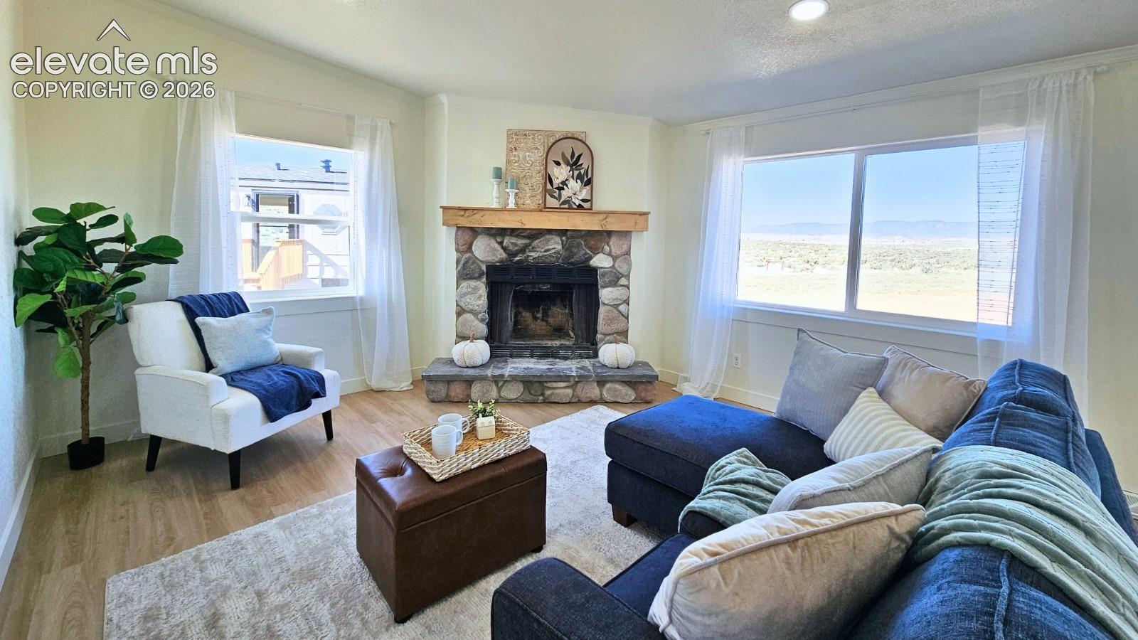Living area featuring wood-finish flooring, a stone-faced fireplace with a natural timber mantel, recessed lighting, and large windows with extensive landscape scenery