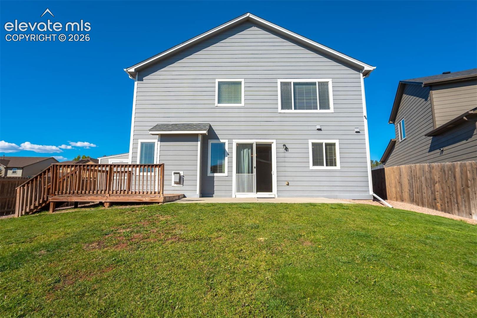 Rear exterior with light gray siding, multiple windows, a ground-level patio, and a wood deck