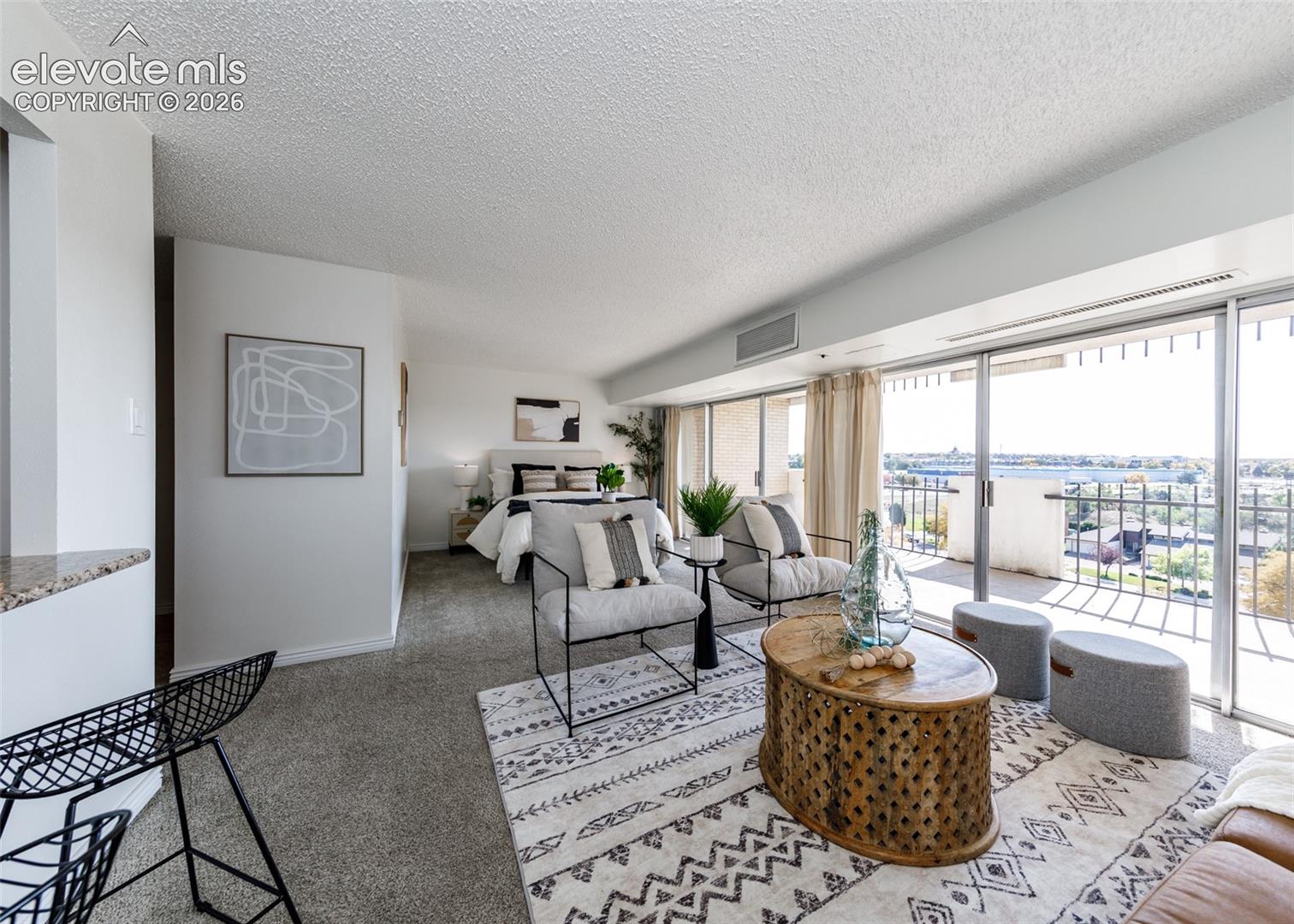 Open-concept living space featuring carpeted flooring, textured ceilings, and a sliding glass door providing external balcony access with metal railings