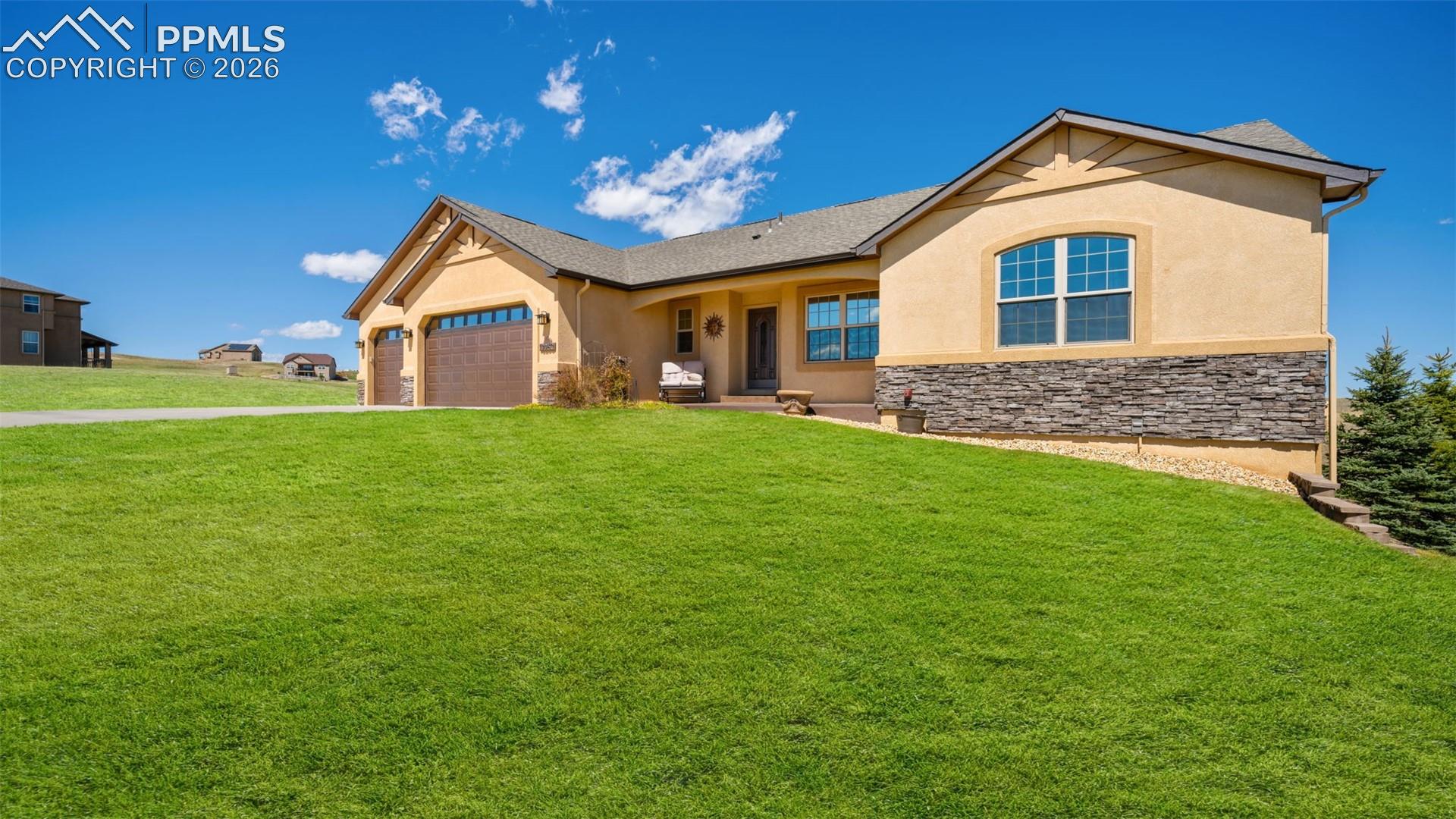 View of front of home with stucco and stone an attached 3 car garage, a front lawn, and driveway