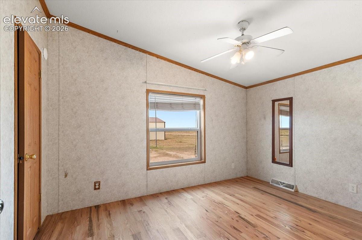 Wood-finish flooring, ceiling fan with integrated lighting, natural light window, paneled walls, and a recessed air vent