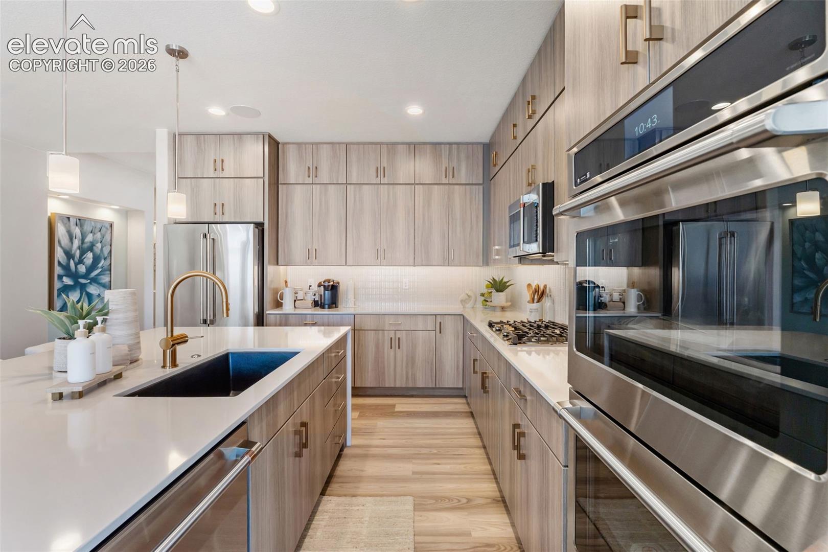 Kitchen featuring light wood-finish cabinetry, stone-surface countertops, a large kitchen island with an undermount sink, built-in stainless steel appliances, and wood-finish flooring
