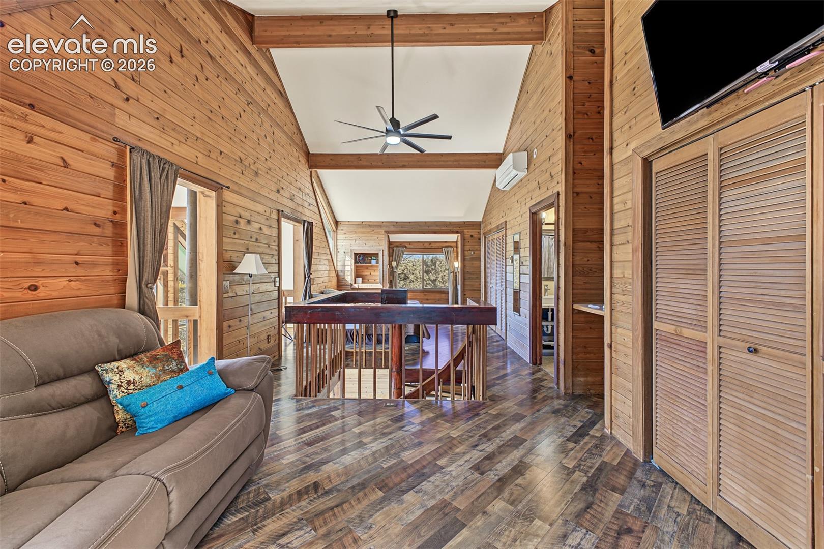 Wood-paneled walls and ceiling, exposed wooden beams, wood-finish flooring, and a ceiling fan