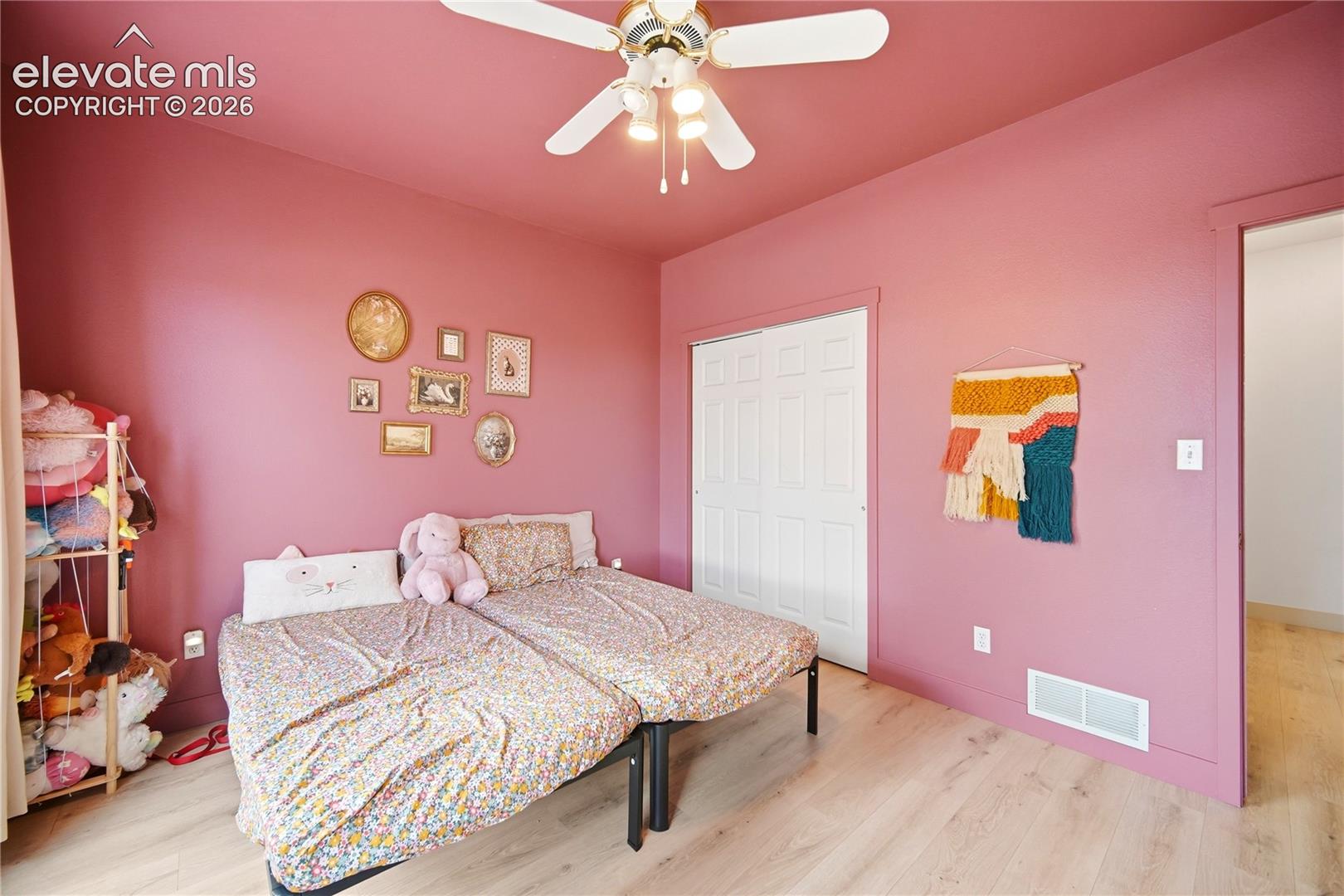 Room featuring wood-finish flooring, a white ceiling fan with integrated lighting, and white bifold closet doors