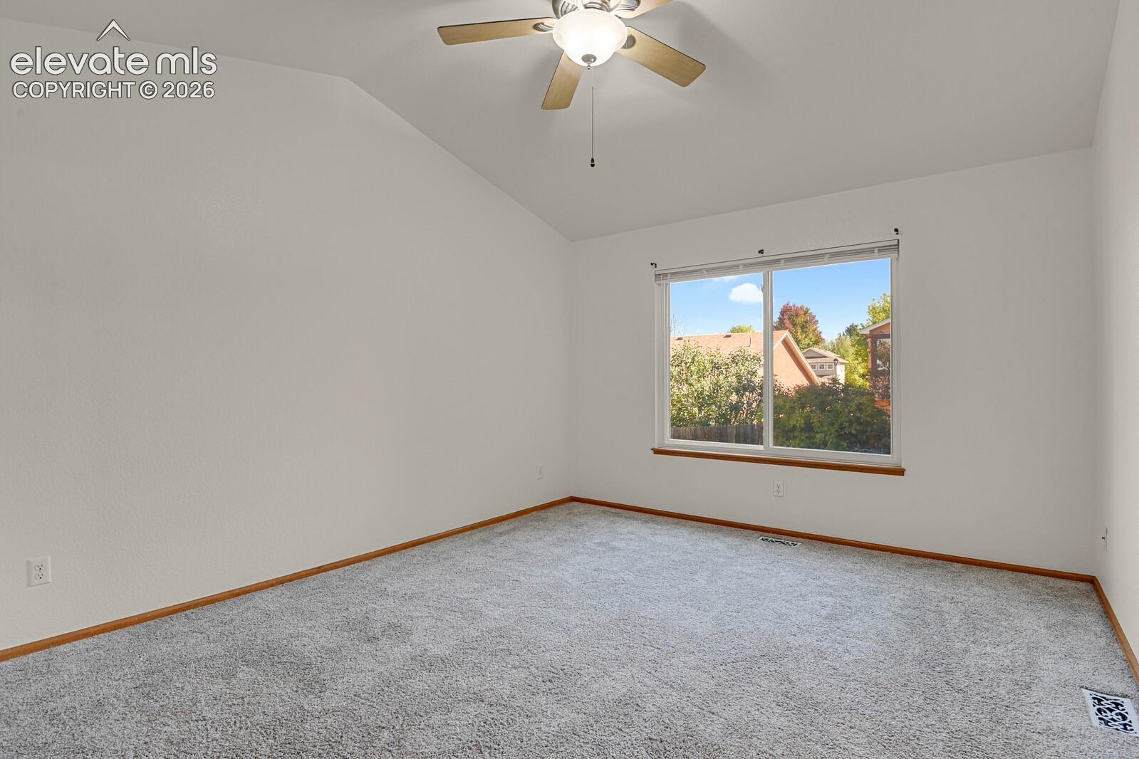 Vaulted ceiling, ceiling fan with integrated lighting, large window with wood-finish sill, neutral-toned carpeting, and white walls