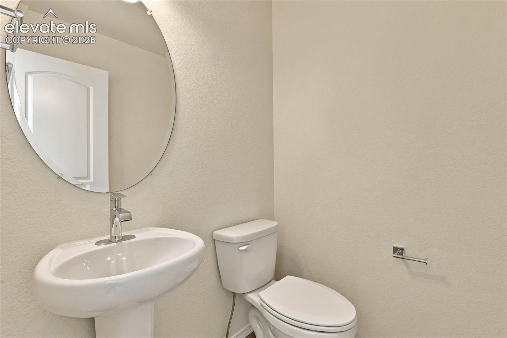 Pedestal sink with a single-handle faucet, oval frameless wall mirror, and dual-flush toilet