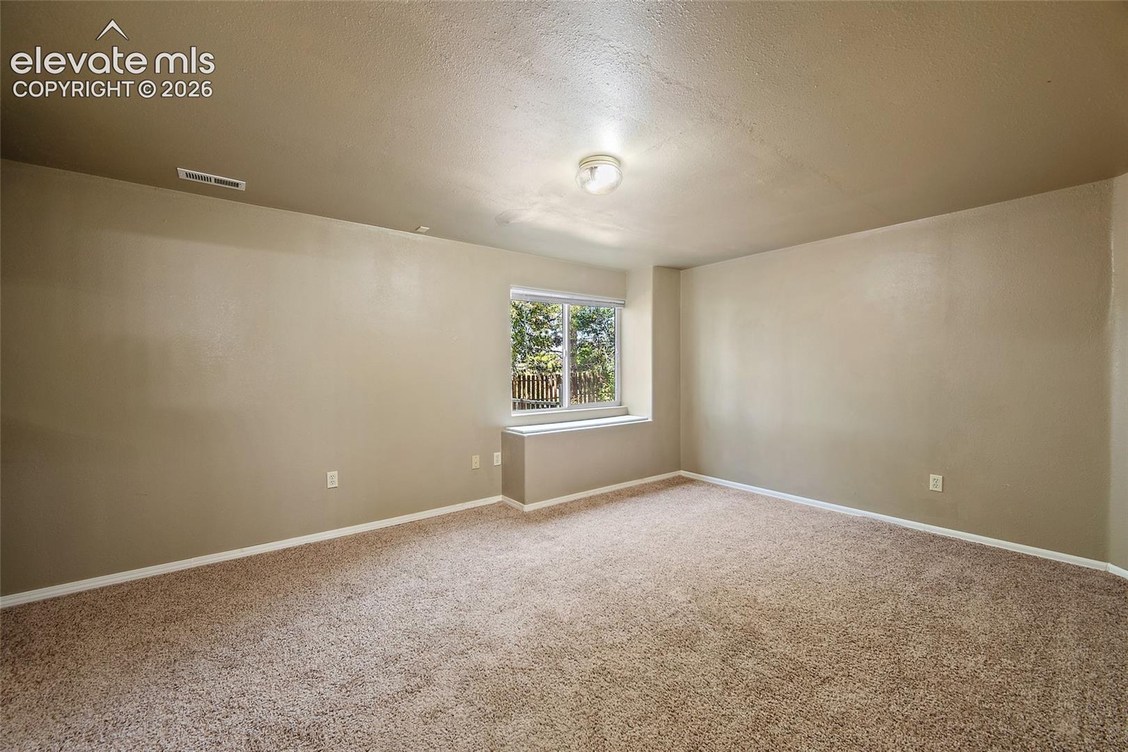 Carpeted room with a window featuring exterior views, neutral wall color, white trim, and a ceiling-mounted light fixture