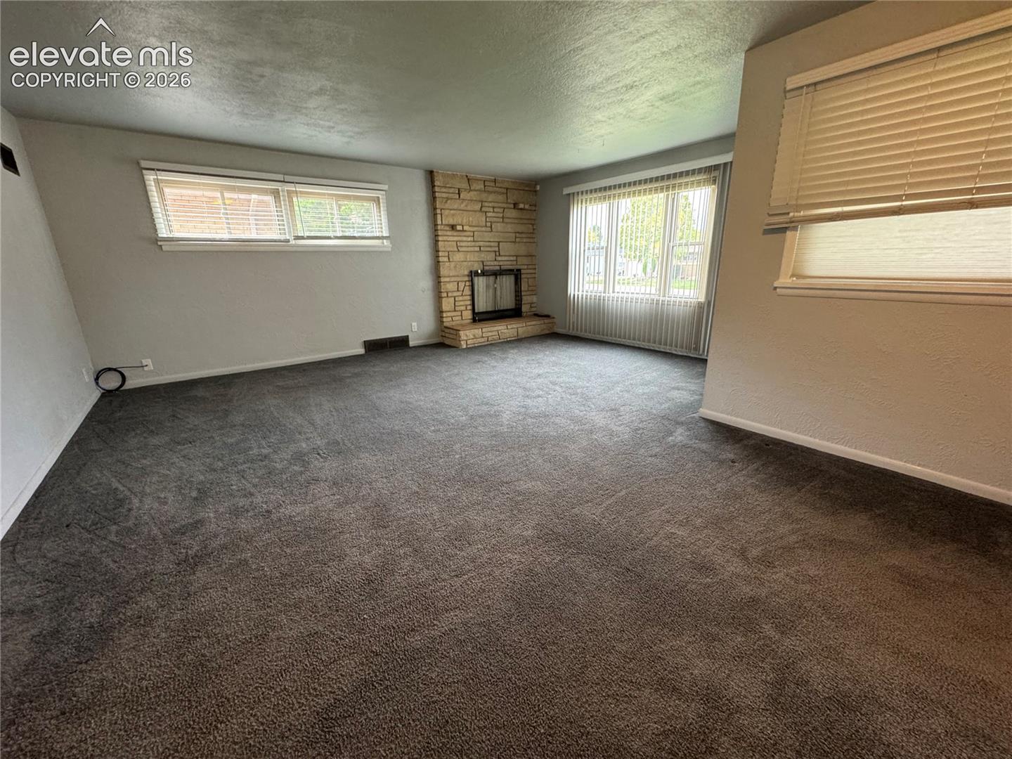 Living area featuring a floor-to-ceiling stone fireplace, wall-to-wall carpeting, and multiple windows with integrated blinds