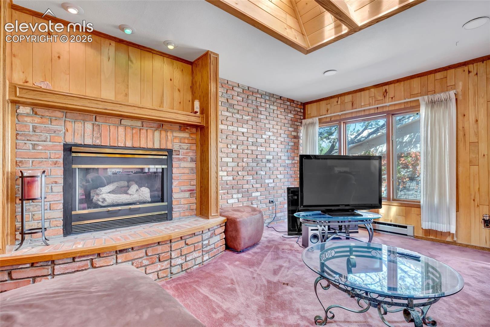 Brick accent wall with a built-in fireplace, wood paneling, and an overhead skylight